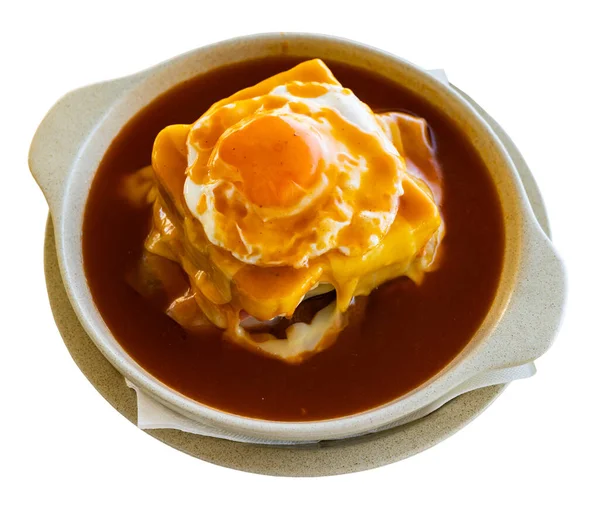 Francesinha, Portuguese sandwich made with bread, ham, fresh sausage, grilled steak, covered with melted cheese and fried egg placed on top, with hot spiced beer sauce. Isolated on white background
