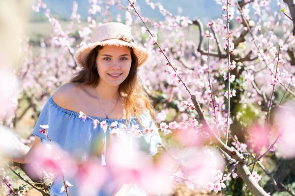 身着蓝色衣服头戴草帽的年轻漂亮女士的画像 她在公园里摆姿势 背景是繁茂的树木 — 图库照片