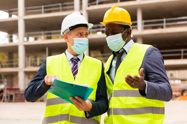 Portrait of an engineer and architect in protective mask with folder of documents at a construction site