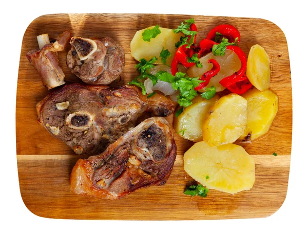 Delicious baked lamb leg slices served with fried potatoes and red pepper sprinkled with chopped fresh parsley on wooden board. Isolated on white background