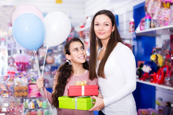 在玩具商店里 高兴的母亲和女儿拿着礼物和气球的画像 注重妇女 — 图库照片