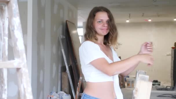 穿着白衬衫和短裤的年轻漂亮的女房东在一个装修过的房间里摆出一副滑稽的姿势 — 图库视频影像