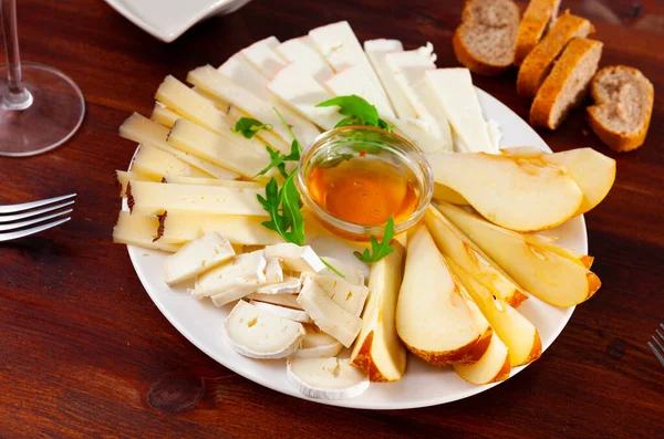 様々な種類のチーズがスライスされ 少し蜂蜜のボウルとプレート上で提供されます — ストック写真
