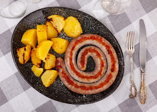 Roasted botifarra, Spanish sausage, cooked with potatoes and served on plate.