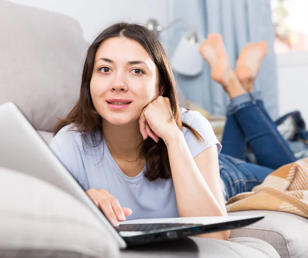 积极的年轻女性在沙发上放松 在家使用笔记本电脑 — 图库照片