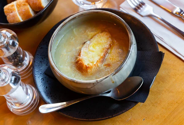 French onion soup served in bowl with crouton and serving pieces.