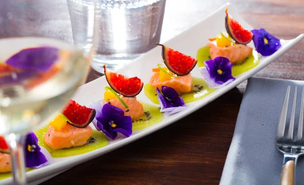 Exotic ceviche of pickled salmon served on circles of fresh kiwi with figs, cumquat, lime zest and blue pansies..