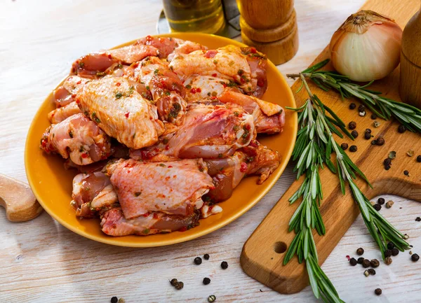 Plate with spicy marinated chicken wings prepared for family picnic on table with condiments and onions