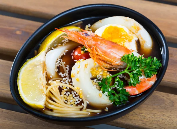 Spicy Pan-Asian soup with squid, shrimp, egg noodles and sesame