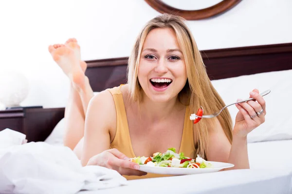 Positive Young Blond Woman Lying Bed Eating Green Salad — Fotografia de Stock