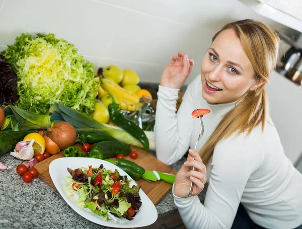 Young woman standing at kitchen top with plate of salad