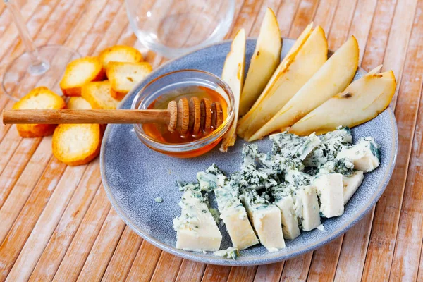 Blue cheese served on plate with slices of pear and honey.