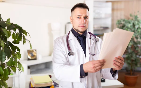 Médico Masculino Casaco Branco Examina Cuidadosamente Documentos Escritório Clínica — Fotografia de Stock