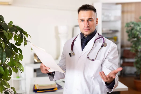 Man doctor standing in office and analyzing documentation in his hands.