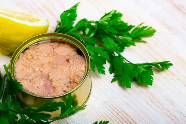 Canned fish, tuna chunks in sunflower oil served with herbs and lemon on wooden table