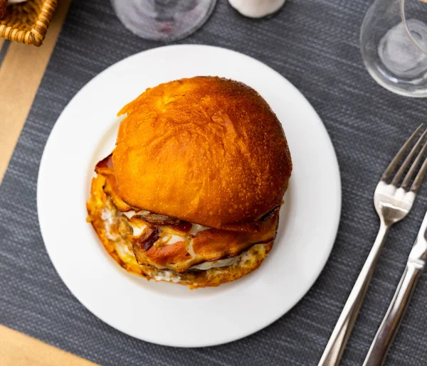 Appetizing cheeseburger with beef patty and fried bacon slices in fluffy bun served on plate. Popular fast food snacks concept..