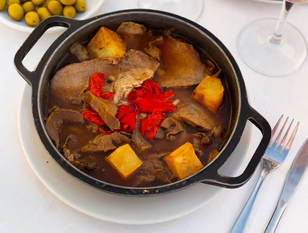 Traditional German braised pork cheeks in brown red wine sauce with mushroom and onions as closeup in a casserole