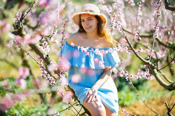 穿着蓝色连衣裙 头戴蓝色帽子的少女在春天花园的桃子里 — 图库照片