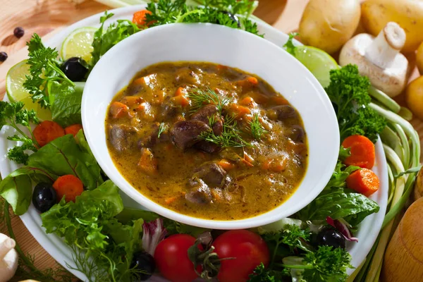 Delicious cooked goulash from chicken hearts served with vegetables and fresh lettuce at plate..