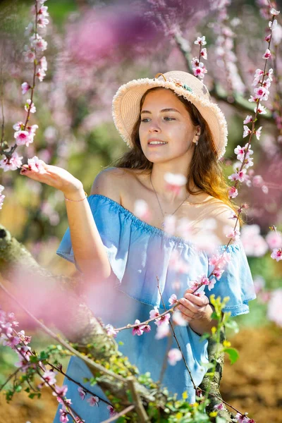 穿着蓝色连衣裙 头戴蓝色帽子的少女在春天花园的桃子里 — 图库照片