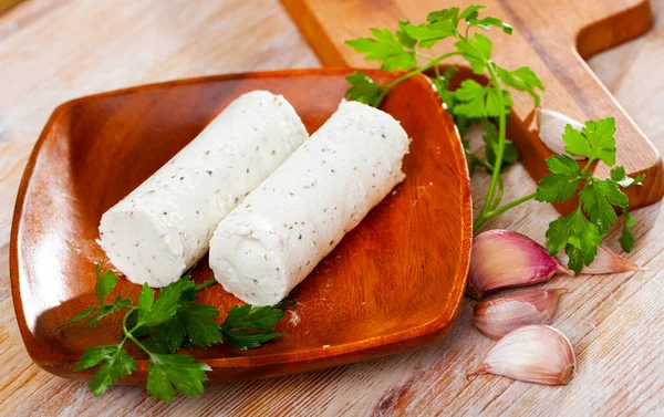 Two small logs from soft spicy goat cheese with herbs and garlic on wooden table