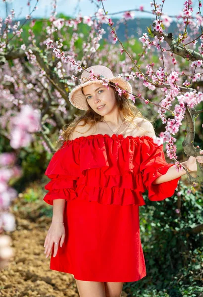 站在春花盛开的花园里 身穿红衣服 头戴草帽 笑容可亲的年轻女郎的画像 — 图库照片