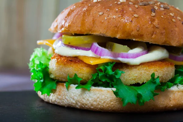 Fresh tasty burger with bread crumb coated fried chicken breast, cheese, lettuce salad, onion and marinated cucumbers