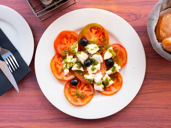 Light refreshing Caprese salad of tender mozzarella and ripe tomatoes with fragrant pesto sauce garnished with pickled olives. Italian style appetizer or entree..