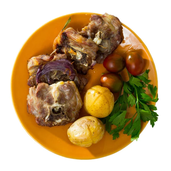 Top view of baked lamb leg chops served on orange dish with baked potatoes, tomatoes and greens. Isolated over white background.