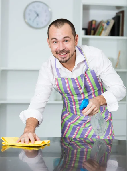 Positiver Junger Mann Schürze Putzt Seinen Schreibtisch Mit Dem Reinigungsmittel — Stockfoto