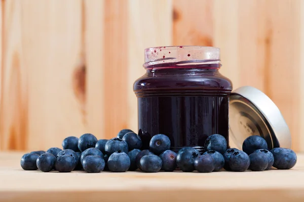 Image of sweet blueberry jam in jar and berries on wooden surface