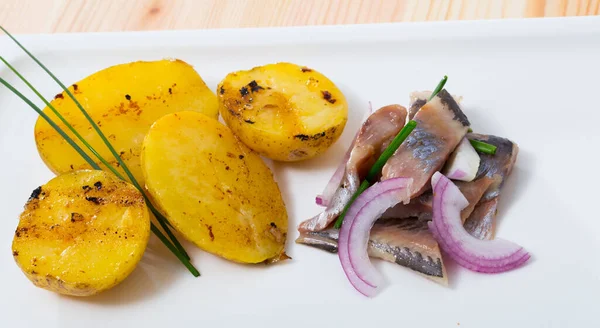 Appetizing slices of low-salted herring with pieces of fried potatoes