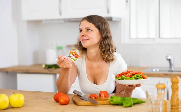 キッチンでテーブルにもたれて調理されたサラダを食べる陽気なヨーロッパの女性の肖像画 食事を楽しむ女 — ストック写真