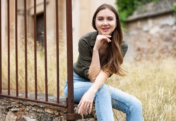 年轻性感的女人在一座废弃的建筑旁边 靠近一个锻造的铁栅栏 — 图库照片