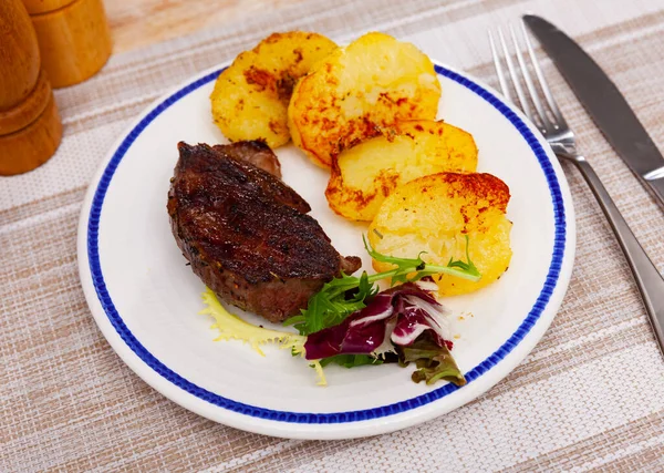 Appetizing grilled beef strip steak served with baked potato slices garnished with greens..