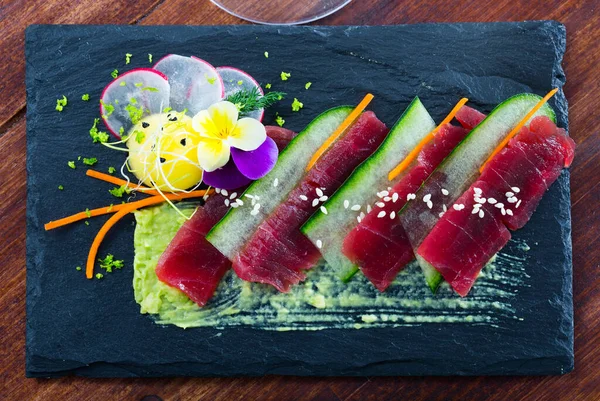 Carpaccio of tuna fish, cucumber, avocado sauce served on slate plate with edible flowers