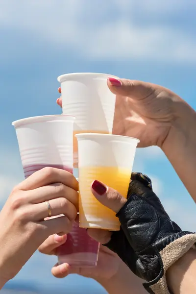 Hands with plastic glasses against the sky — Stock Photo, Image