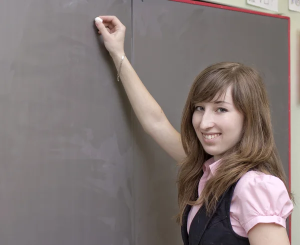 De jonge mooie vrouw schrijft een krijt op een bord van de school — Stockfoto