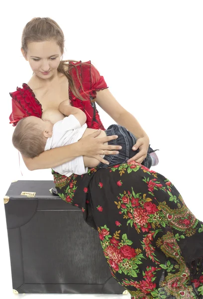 Мать кормит грудью своего ребенка, сидя на чемодане — стоковое фото