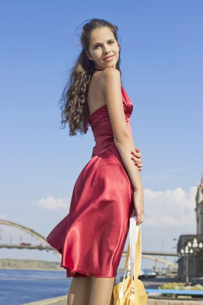 Het meisje in een rode jurk, met een gele zak tegen de hemel — Stockfoto