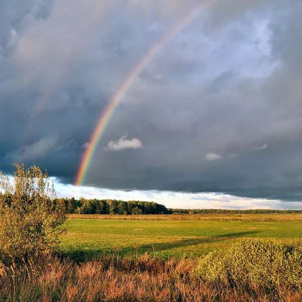 Natural rainbow over autumn field and dark sky. — Stock Photo, Image