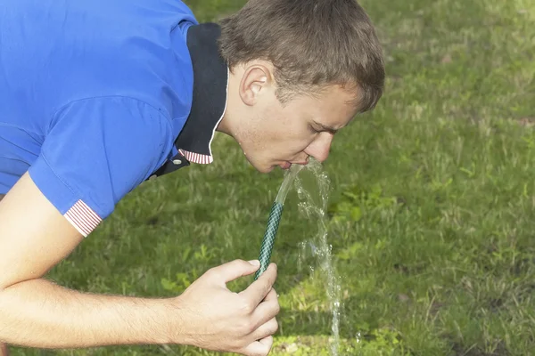 Niño bebe agua de una manguera — Foto de Stock