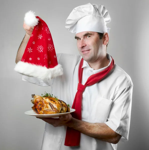Chef showing plate with chicken and Santa hat — Stock Photo, Image