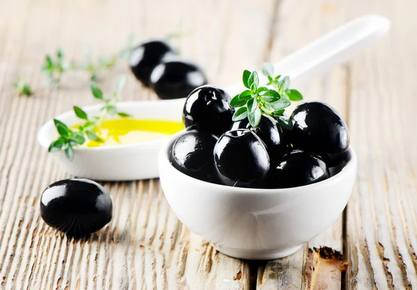 Czarnych oliwek i oliwy z oliwek na drewnianym stołem — Zdjęcie stockowe