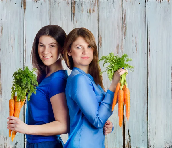 Jóvenes mujeres sonrientes sostiene racimo de zanahorias — Foto de Stock