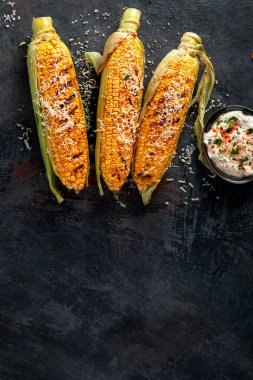 Koyu arkaplanda peynirli ızgara mısır koçanı. Yemek konseptini hasat et. Üst görünüm, düz görünüm, kopyalama alanı