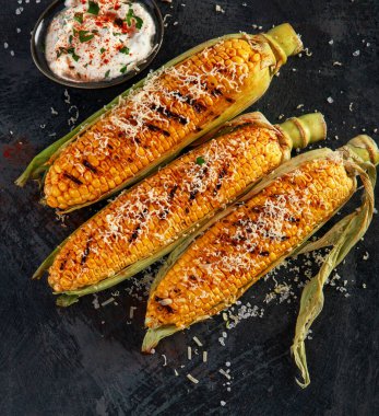 Koyu arkaplanda peynirli ızgara mısır koçanı. Yemek konseptini hasat et. Üst görünüm, düz görünüm, kopyalama alanı