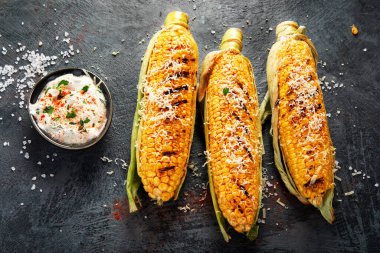 Koyu arkaplanda peynirli ızgara mısır koçanı. Yemek konseptini hasat et. Üst görünüm, düz görünüm, kopyalama alanı