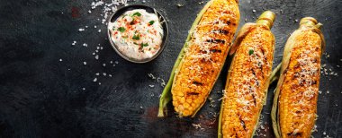 Koyu arkaplanda peynirli ızgara mısır koçanı. Yemek konseptini hasat et. Üst görünüm, düz görünüm, kopyalama alanı, panorama