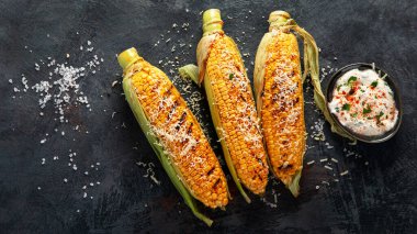 Koyu arkaplanda peynirli ızgara mısır koçanı. Yemek konseptini hasat et. Üst görünüm, düz görünüm, kopyalama alanı